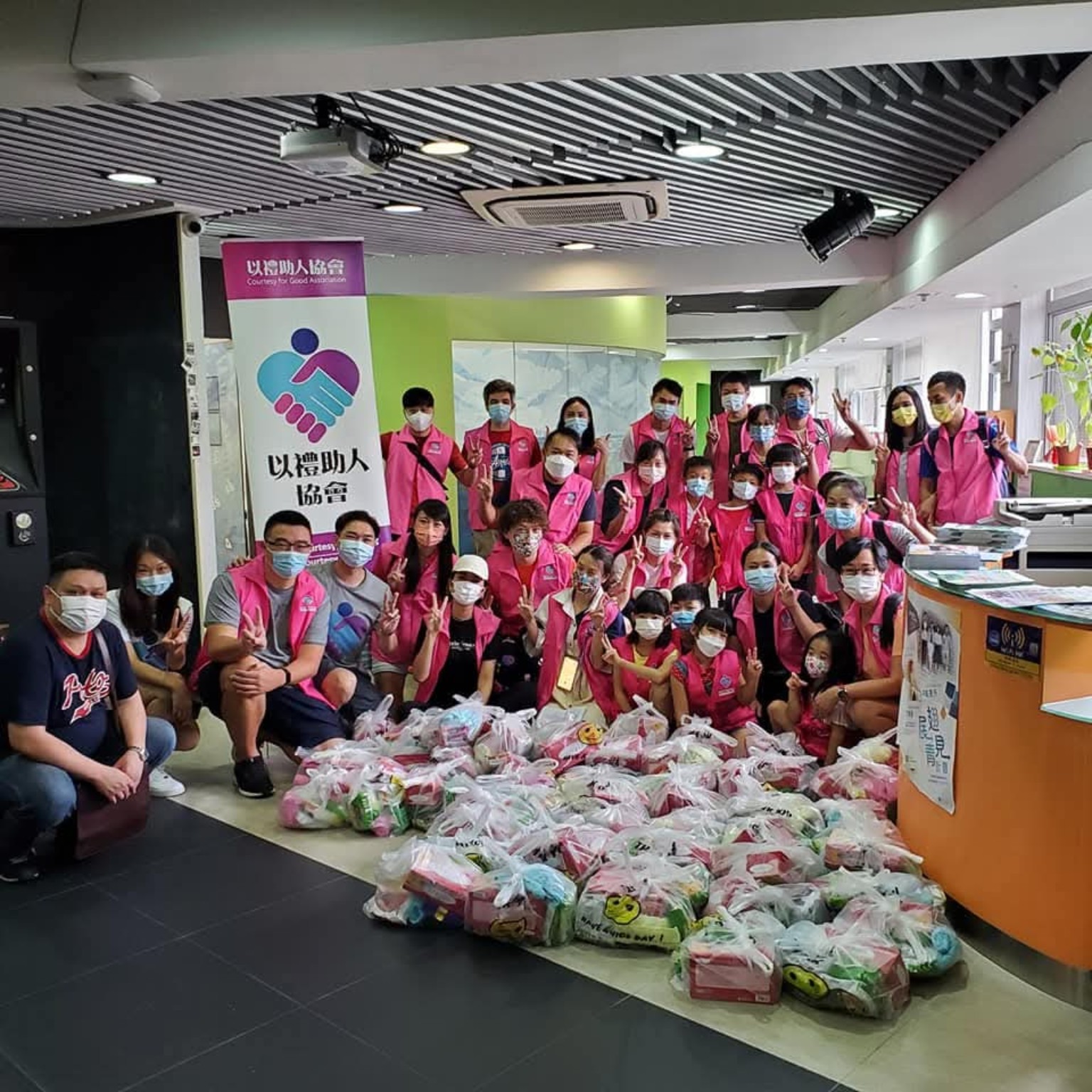 Adult and young volunteers wearing Association vests pose with donated supplies.