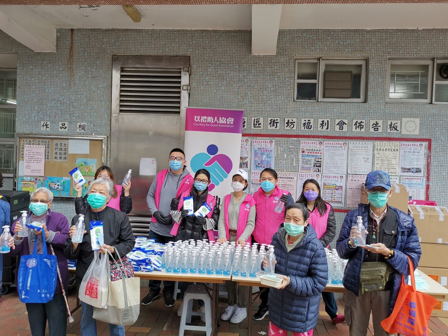 Volunteers and older people display hand sanitiser and disinfectant wipes at a community activity.