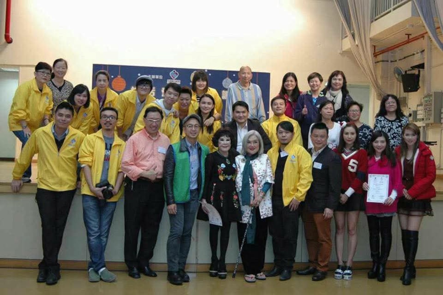Volunteers and participants pose together on a stage at an event venue.