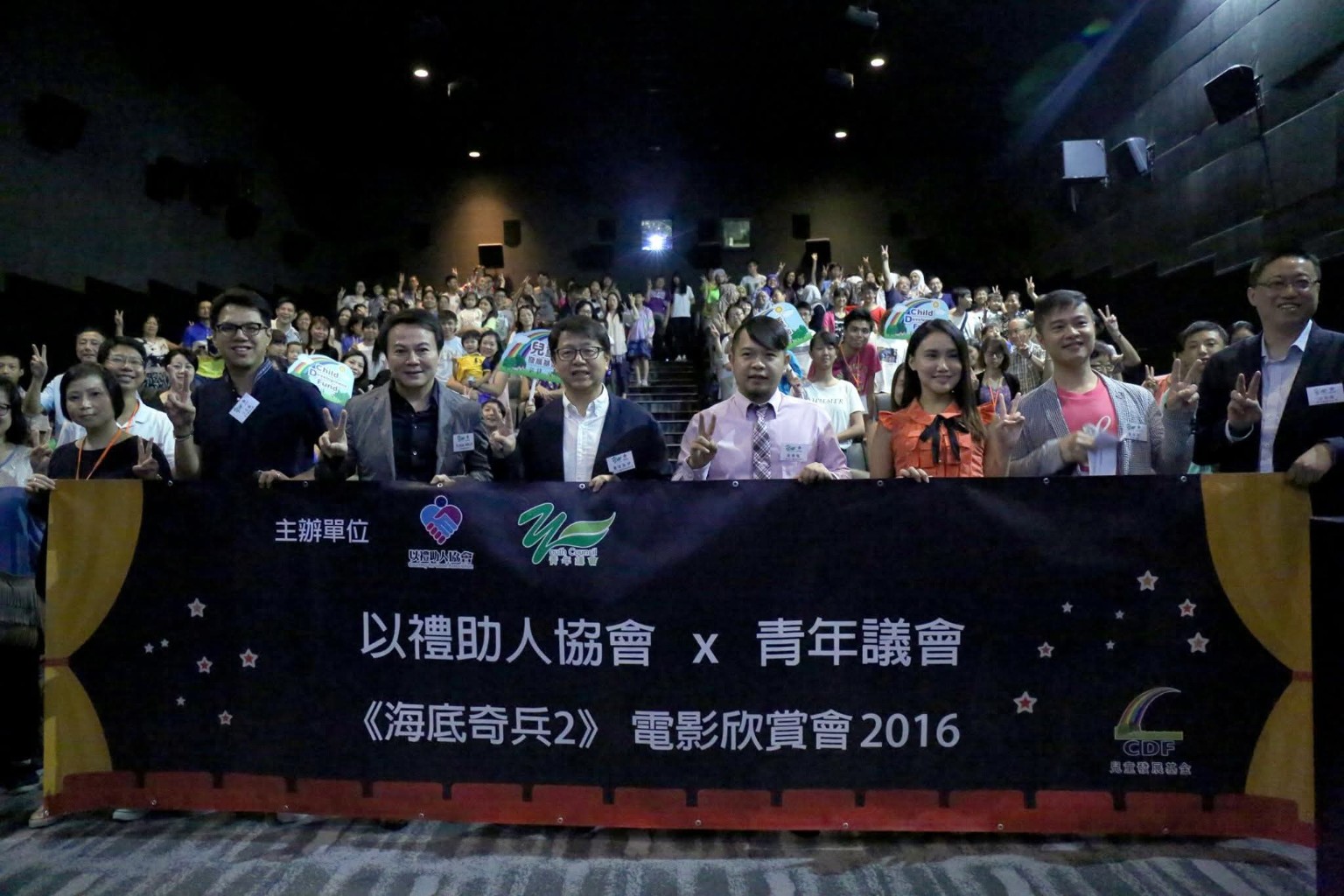 Children, parents and volunteers hold an event banner for a group photo in a cinema.