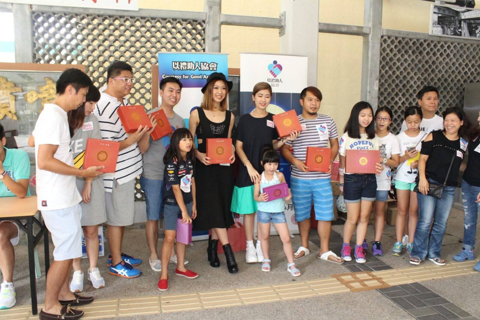 Participants hold festive gift boxes for a group photo in front of Association banners.