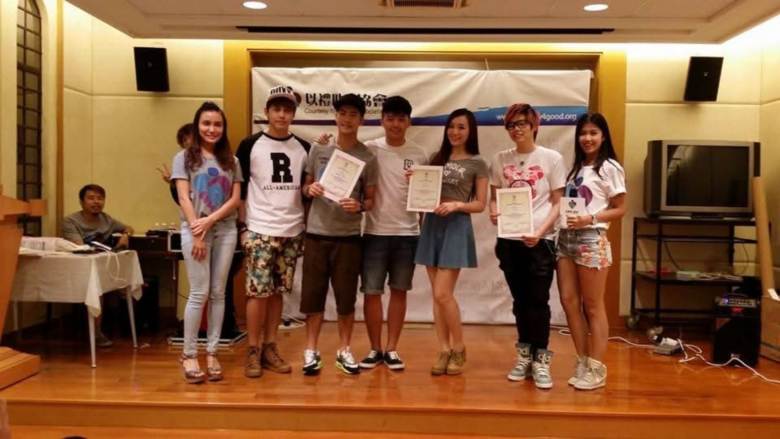 Participants hold certificates for a group photo in front of an Association banner.