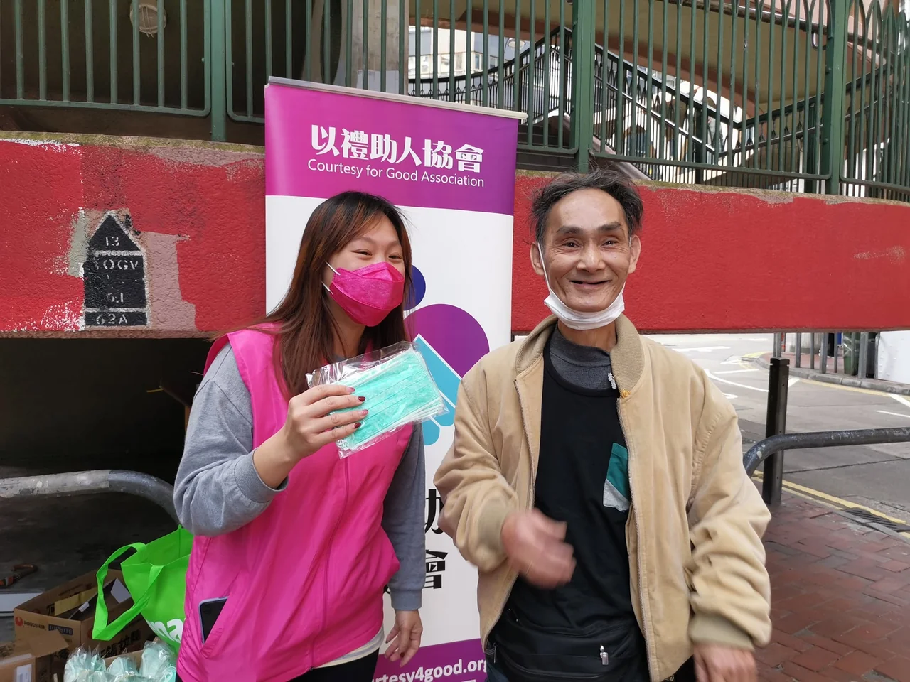 義工在街頭派發口罩，與參與者交流及合照；場地可見以禮助人協會易拉架。